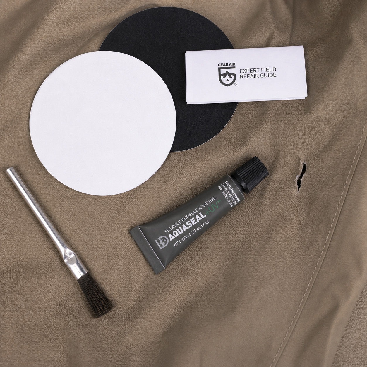 Gear Aid Aquasure FD Repair Kit – obsah sady položený na brodiacich nohaviciach vedľa poškodenej časti materiálu