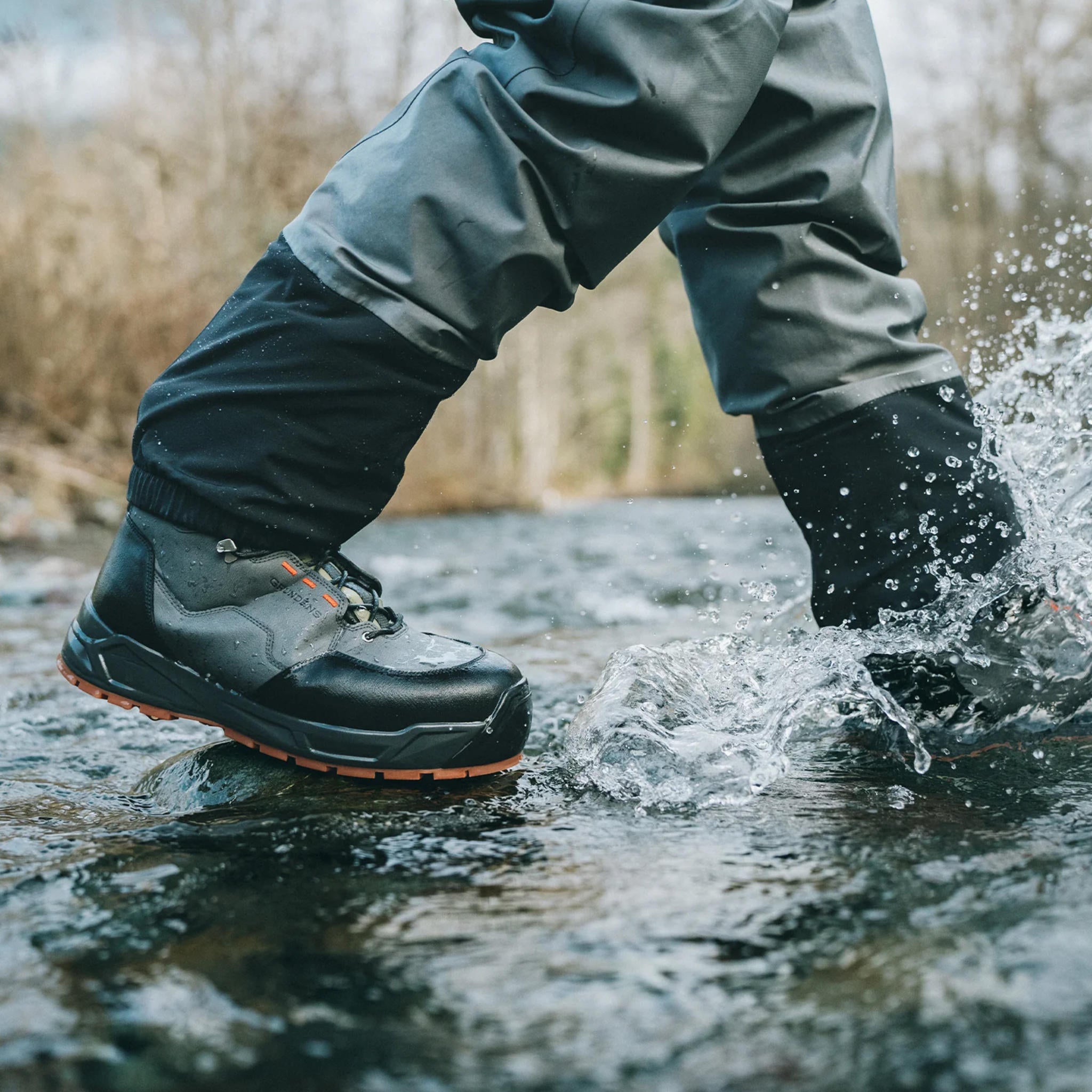 Angler wading in a river wearing dark grey Grundens Boundary wading boots, action shot.